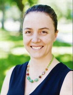 Dr. Moyers in a blue shirt and dark hair pulled back smiling in front of a blurred green background