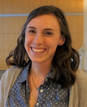 Dr. Smukowski Heil in a blue button up and gray sweater with shoulder length wavy brown hair smiling at the camera